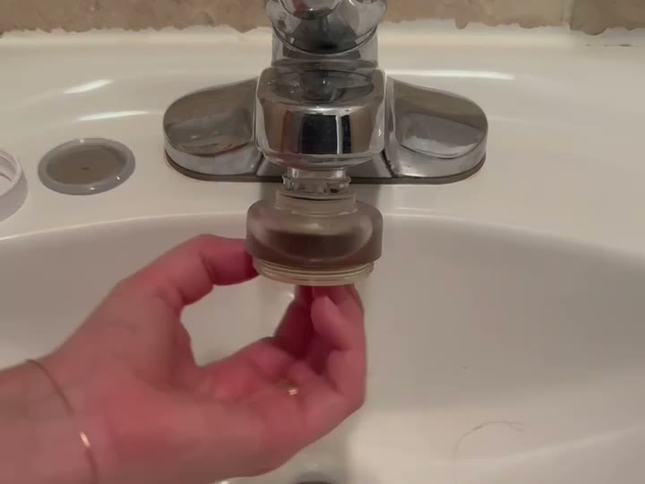 Hand pulling the used cartridge out of a Helios Sink Filter on a faucet, with the bottom cap set on the sink