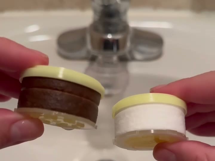 A brown used cartridge held next to a clean new cartridge